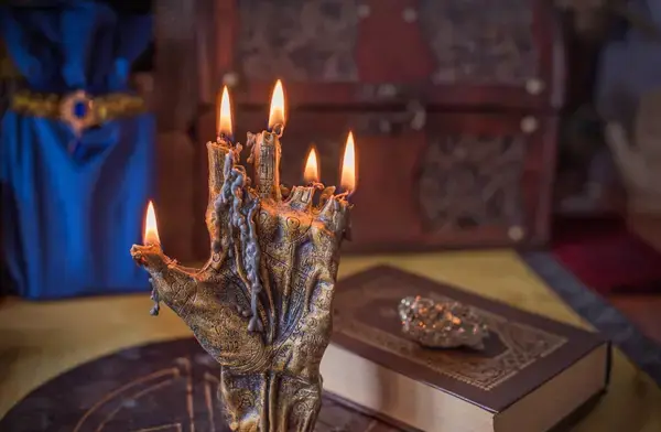 Candelabro en forma de mano con cinco velas encendidas junto a un libro